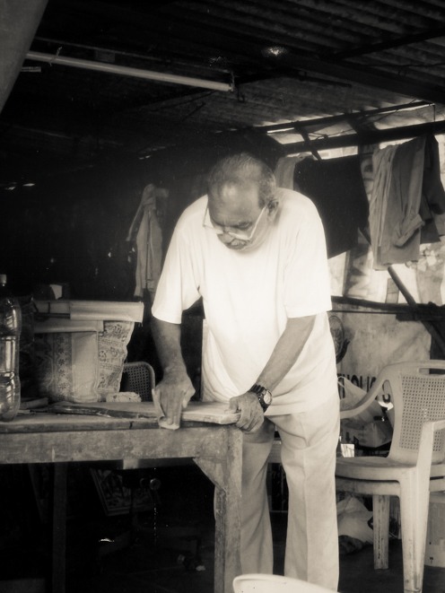 a carpenter (my dad) in a woodshed, sanding a piece of wood with his callused hands