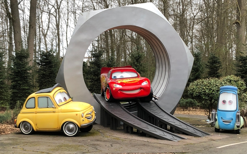 image of three large anthromorphic cars. left yellow, centre red and right blue. the centre car is raised on a dias ringed by a giant mechanical nut. the cars are all smiling.